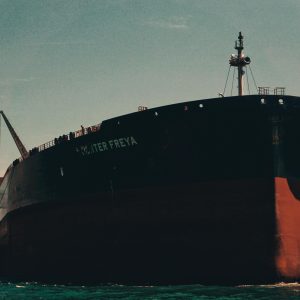 A massive cargo ship named Hunter Freya anchored at a bustling sea port under a clear sky.